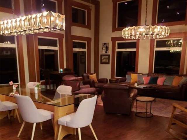 A high-ceilinged dining room and living room area with dark wooden flooring and walls
